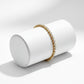 Gold and pearl bracelet on a white cylindrical stand against a light gray background