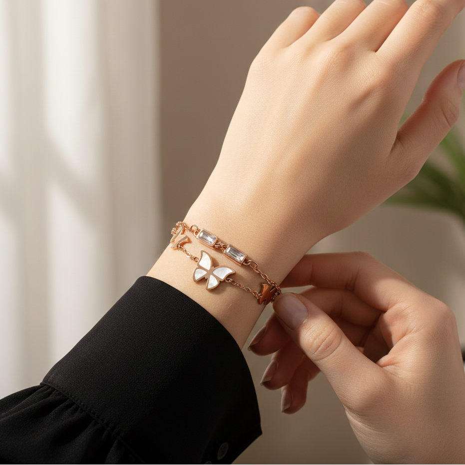 Hand wearing a butterfly-themed bracelet with another hand adjusting it against a neutral background
